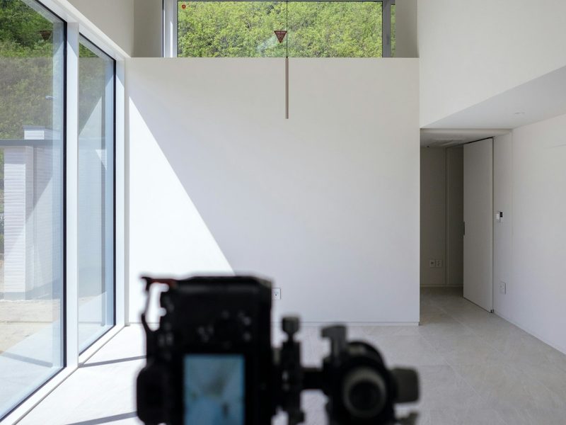 A camera on a tripod photographing a bright, empty room