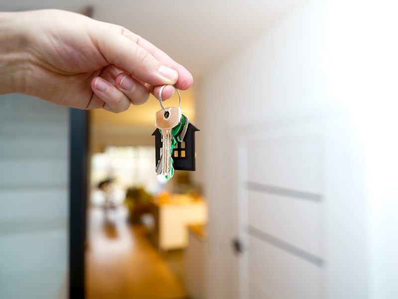 A hand holding keys on a house keyring at an apartment entrance